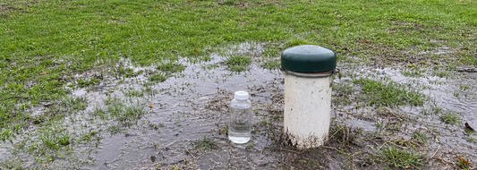 Private well in a flooded U.S. yard with a water sample bottle