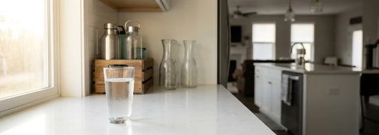 A bright U.S. kitchen counter with a clear glass of water and no visible water filter, lifestyle photo for a 5-gallon jug alternative guide