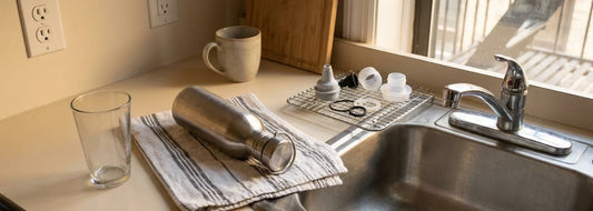Apartment kitchen counter with a clean water glass and washed pitcher lid drying near the sink