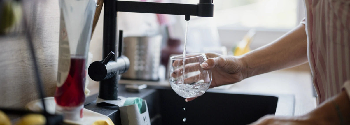 Person filling a glass at a kitchen sink for a reverse osmosis filter replacement guide