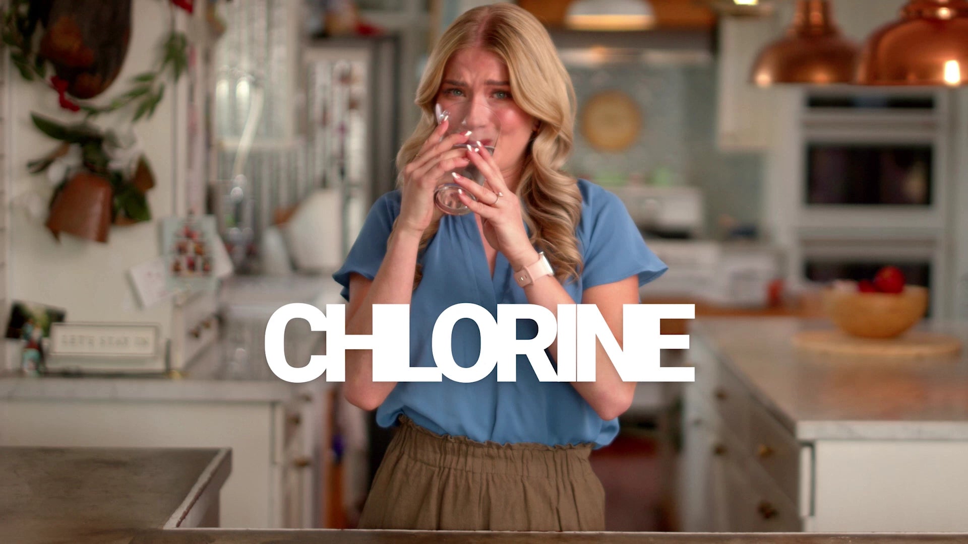Woman in a kitchen holding a glass of water with the word 'CHLORINE' displayed.