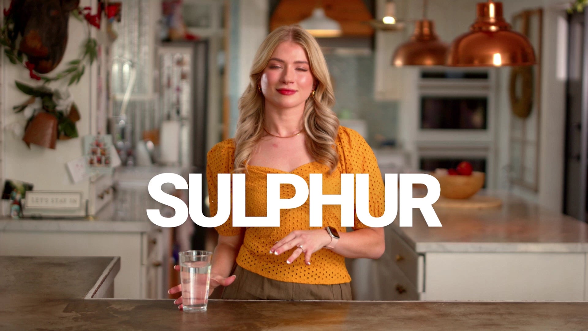 Woman holding a glass of water in a kitchen with 'SULPHUR' text overlay