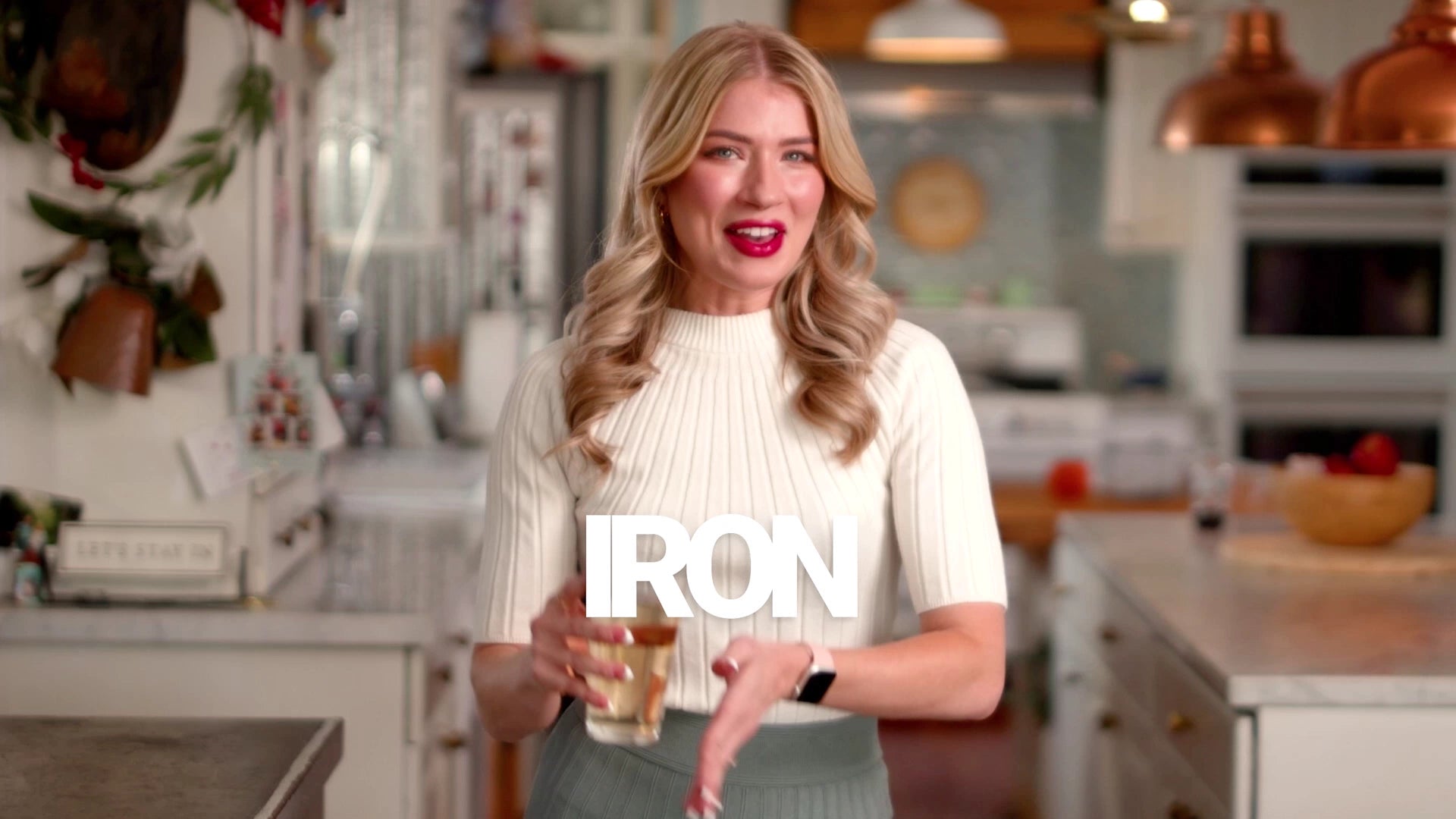 Woman holding a glass and a sign with 'IRON' in a kitchen setting