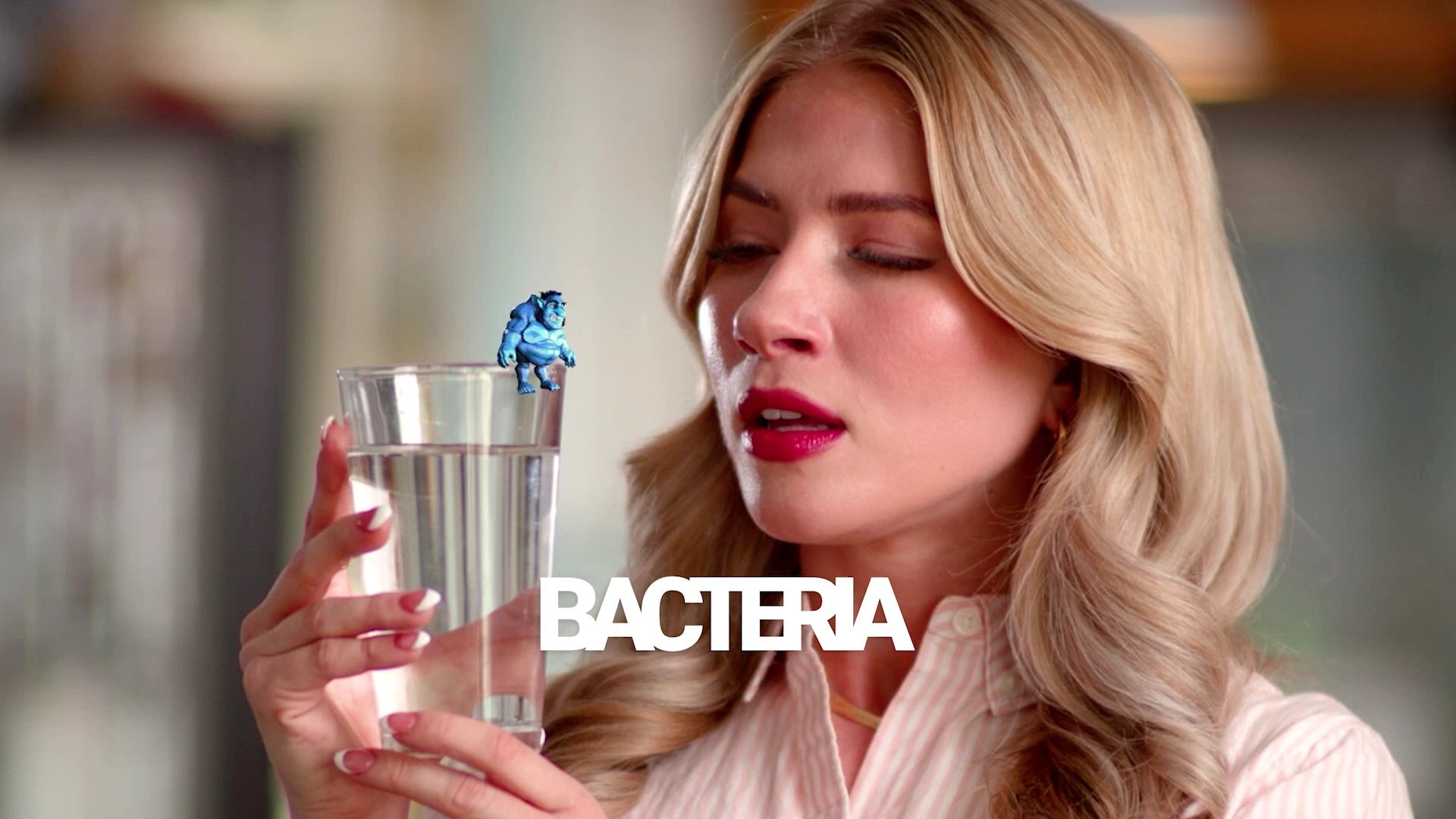 Woman holding a glass of water with a blue bacterium floating above it, set against a blurred indoor background.