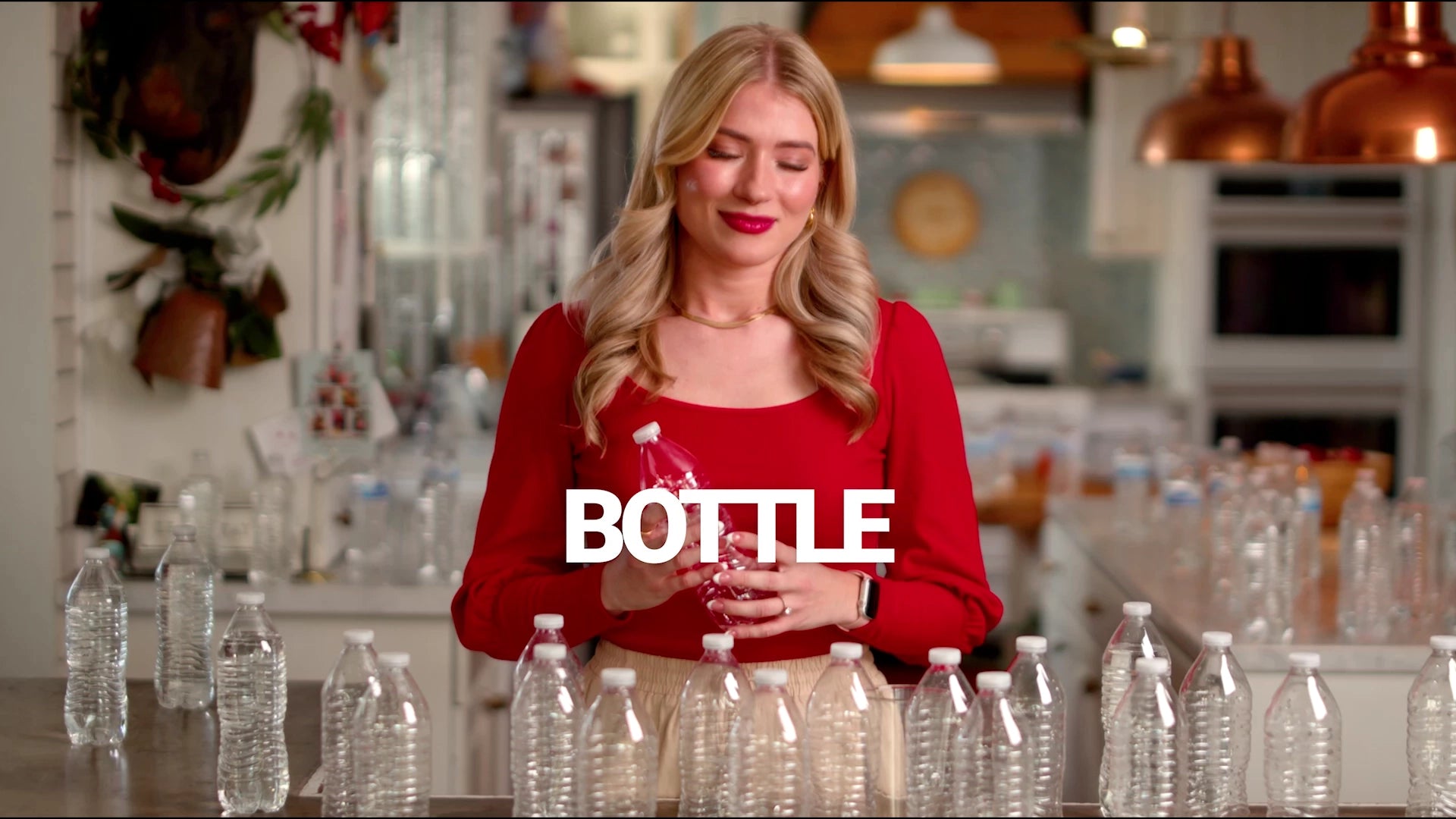 Woman in a red sweater holding a bottle with 'BOTTLE' text in a kitchen setting