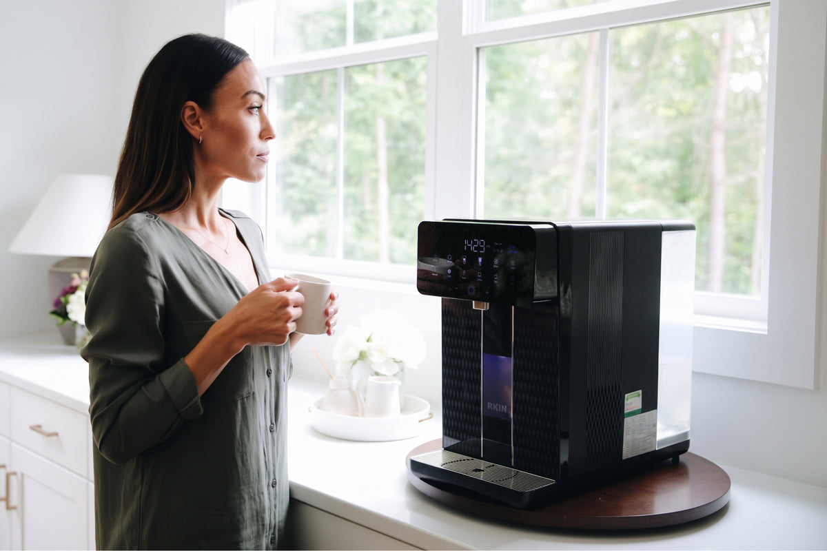 Woman holding a mug next to the RKIN U1 countertop water system in a bright kitchen